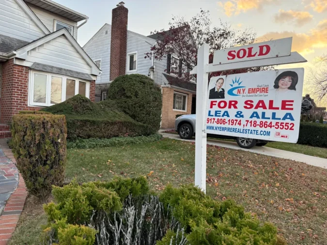 A row of suburban homes with a for-sale sign and overcast sky