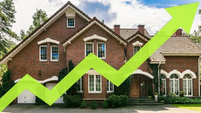 Calculator beside a model house and coins showing higher mortgage costs for homebuyers