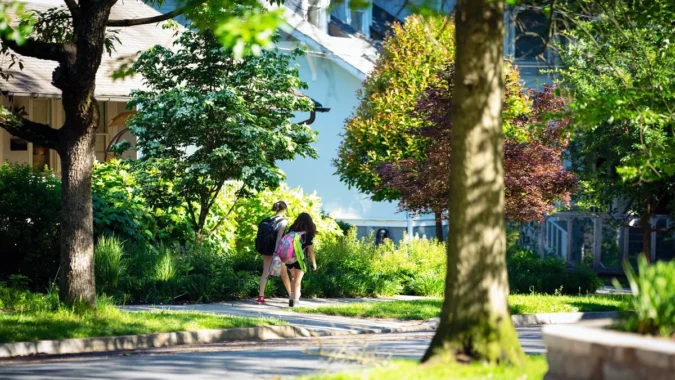 Families walking along a neighborhood sidewalk near a school