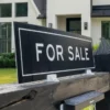 A home for sale sign in front of a suburban house with mortgage rate figures overlaid